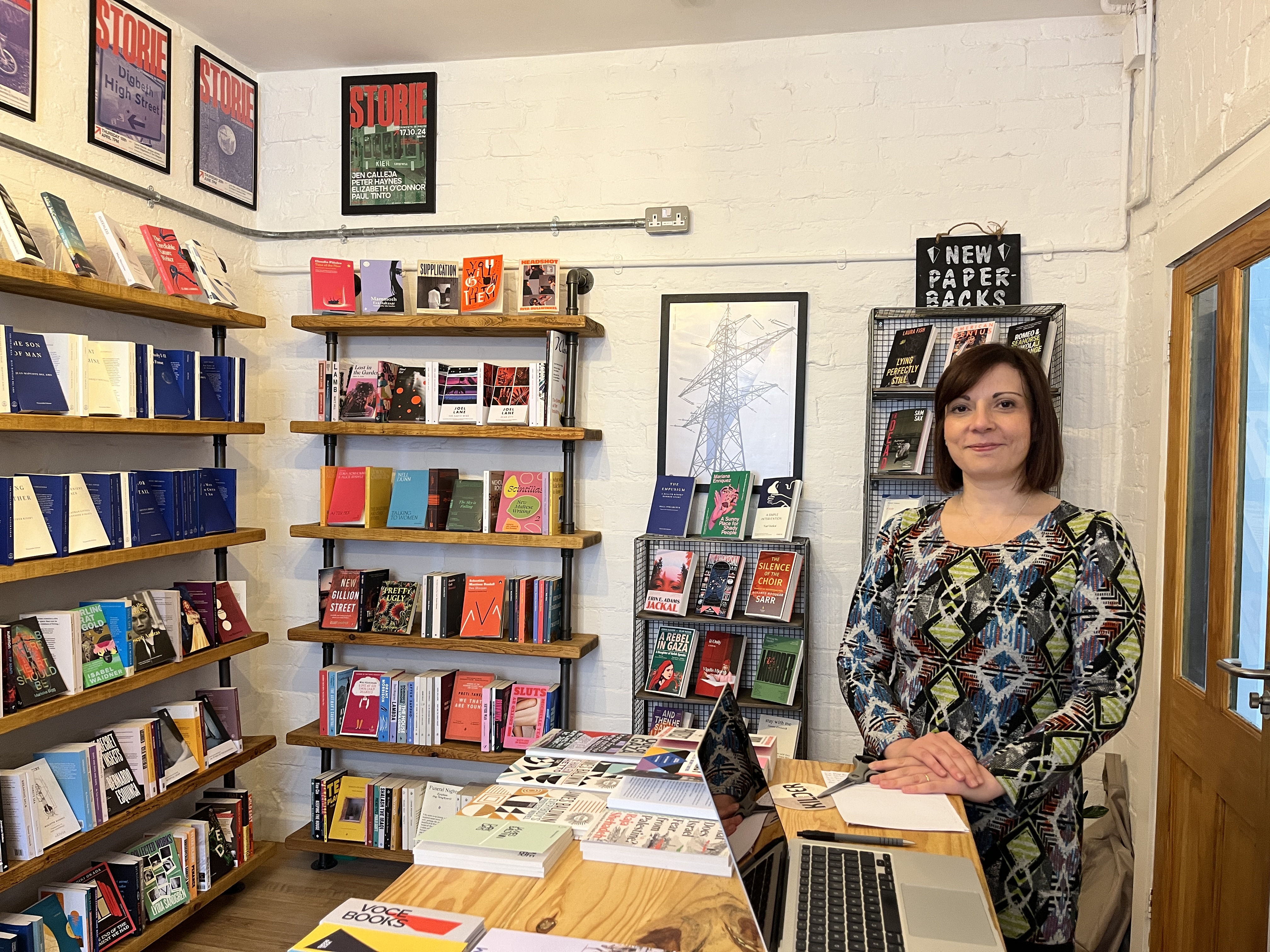 books at the voce bookshop and a white woman with brown hair in front of one of the shelves