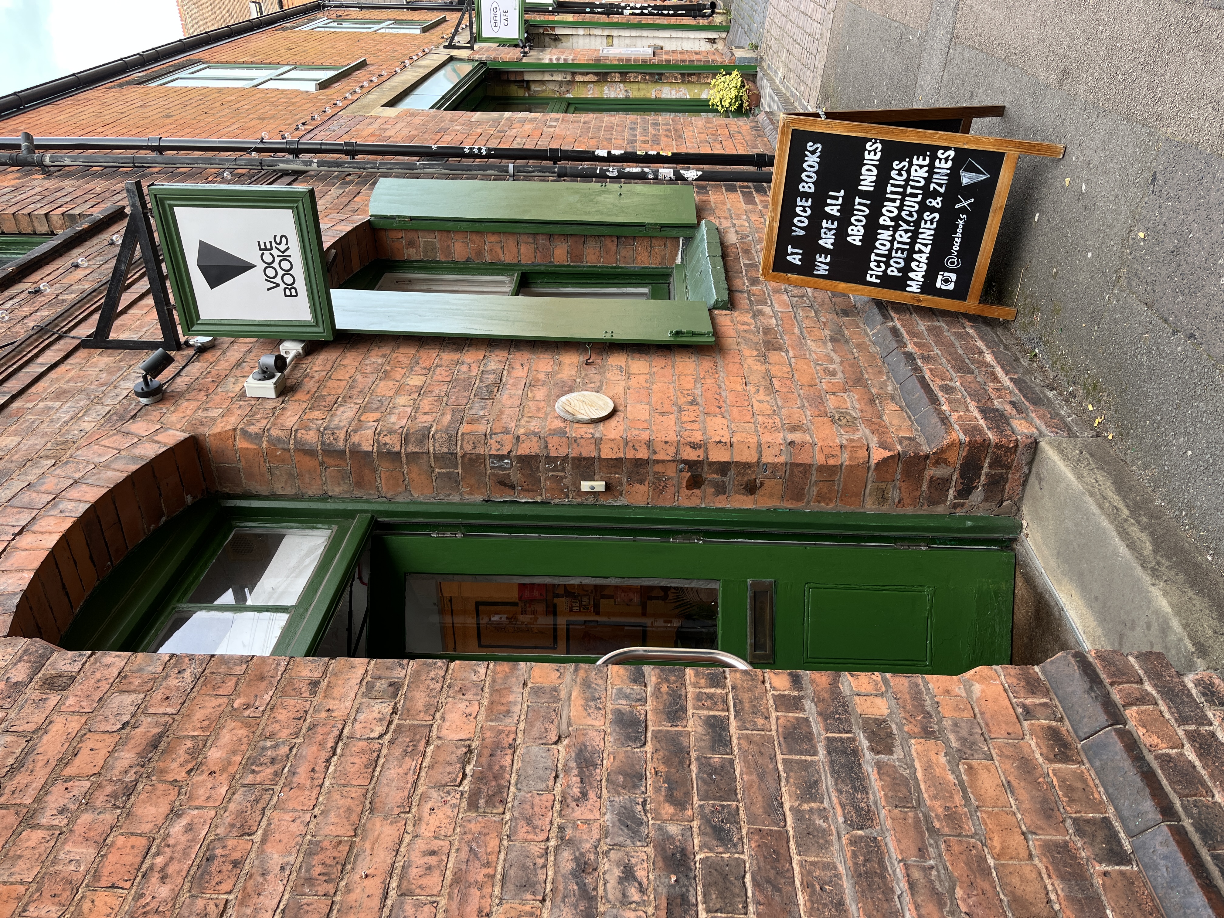 a brick wall with green door and shutters, a display in front of it giving some information about the bookshop voce books